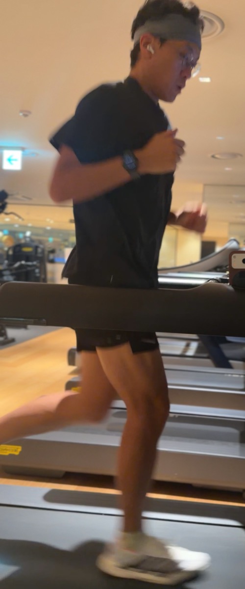 헬스장 트레드밀에서 달리는 러너를 옆에서 촬영한 사진. 트레드밀 손잡이 끝에 휴대폰이 세워져 있다